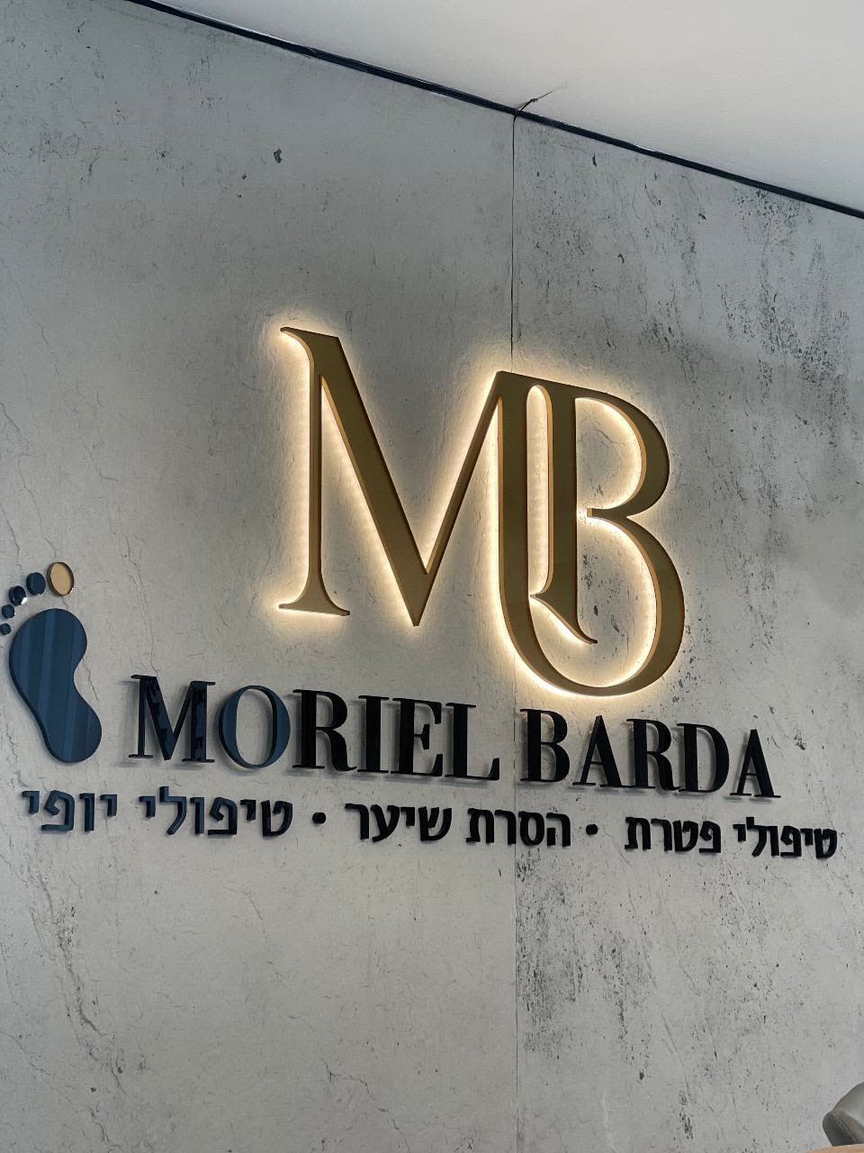 שילוט הקליניקה של מוריאל ברדה — לוגו MB מואר בזהב על קיר בטון